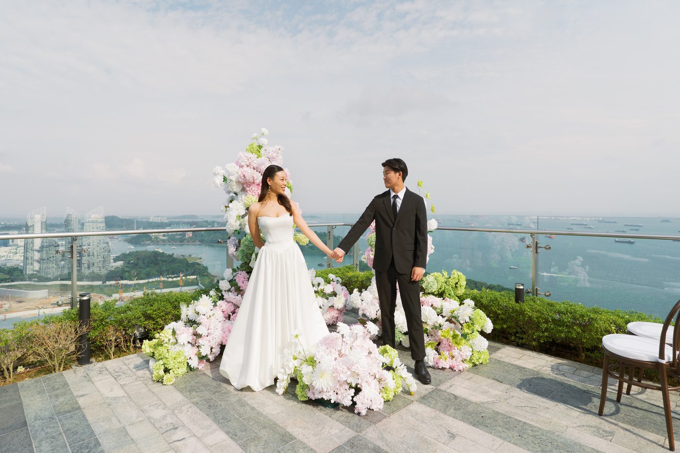 Couple exchanging vows at a rooftop floral arch at 1-Alfaro with views over Sentosa and the sea