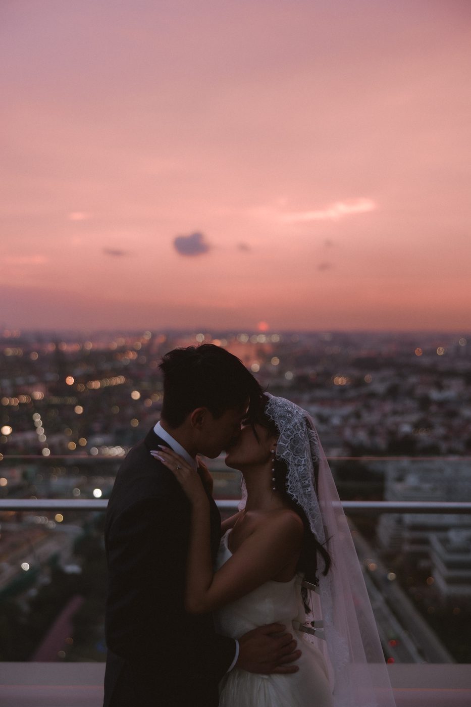 Newlyweds kissing at sunset above the Singapore city lights at 1-Alfaro rooftop wedding venue